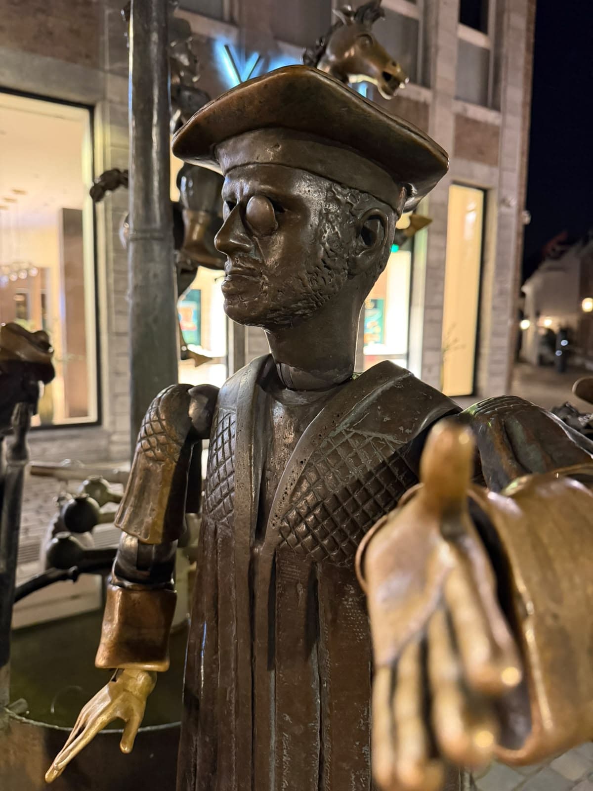 Bronzefigur mit Brille und Hut vor einem beleuchteten Schaufenster
